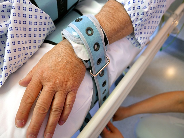 Das Handgelenk einer älteren Person ist an einem Krankenhausbett fixiert.
